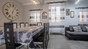 A dining area with a long table, chairs, a large wall clock, and a sofa.