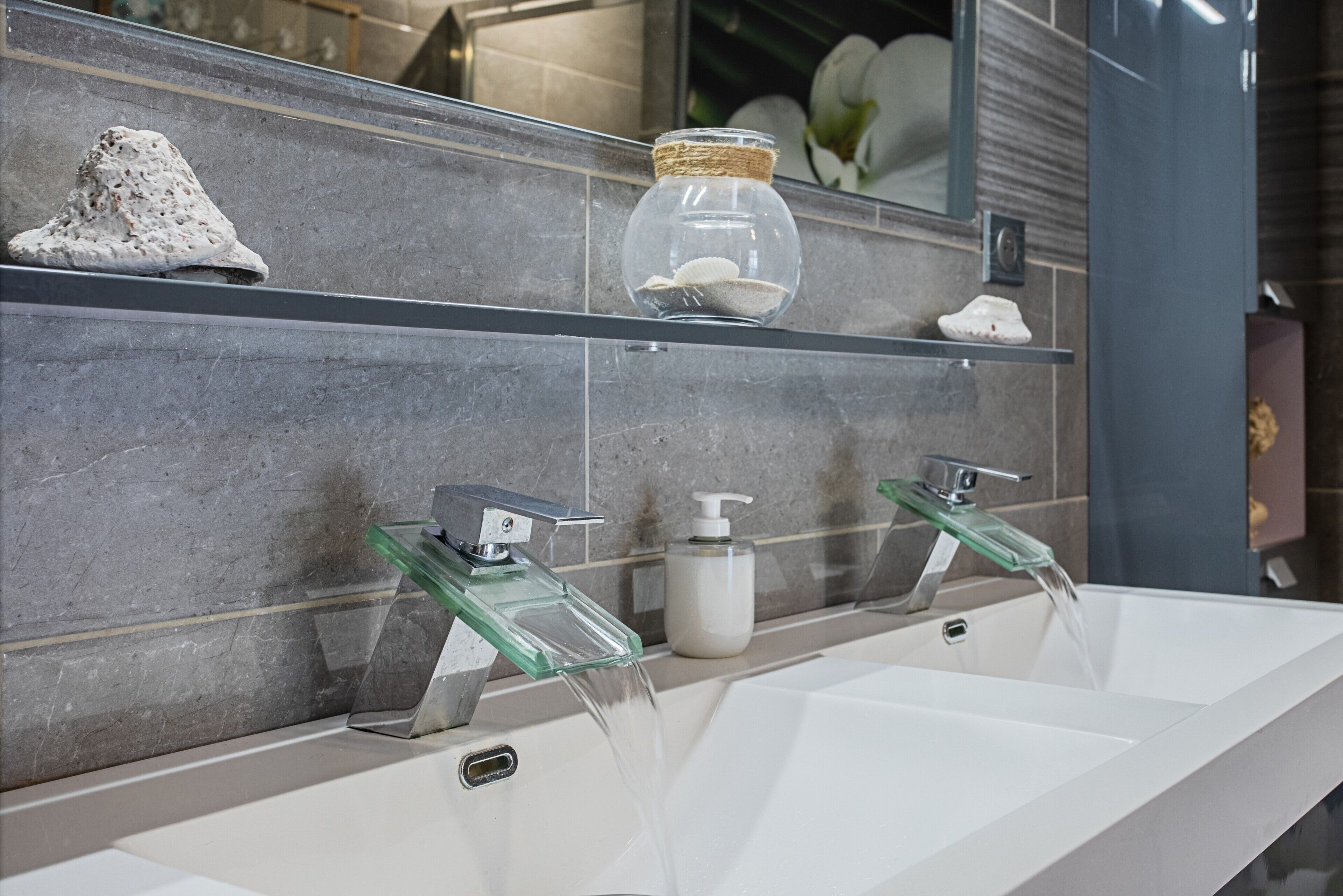 Un bagno con un lavandino bianco, due specchi con rubinetti in vetro e un dispenser per sapone.