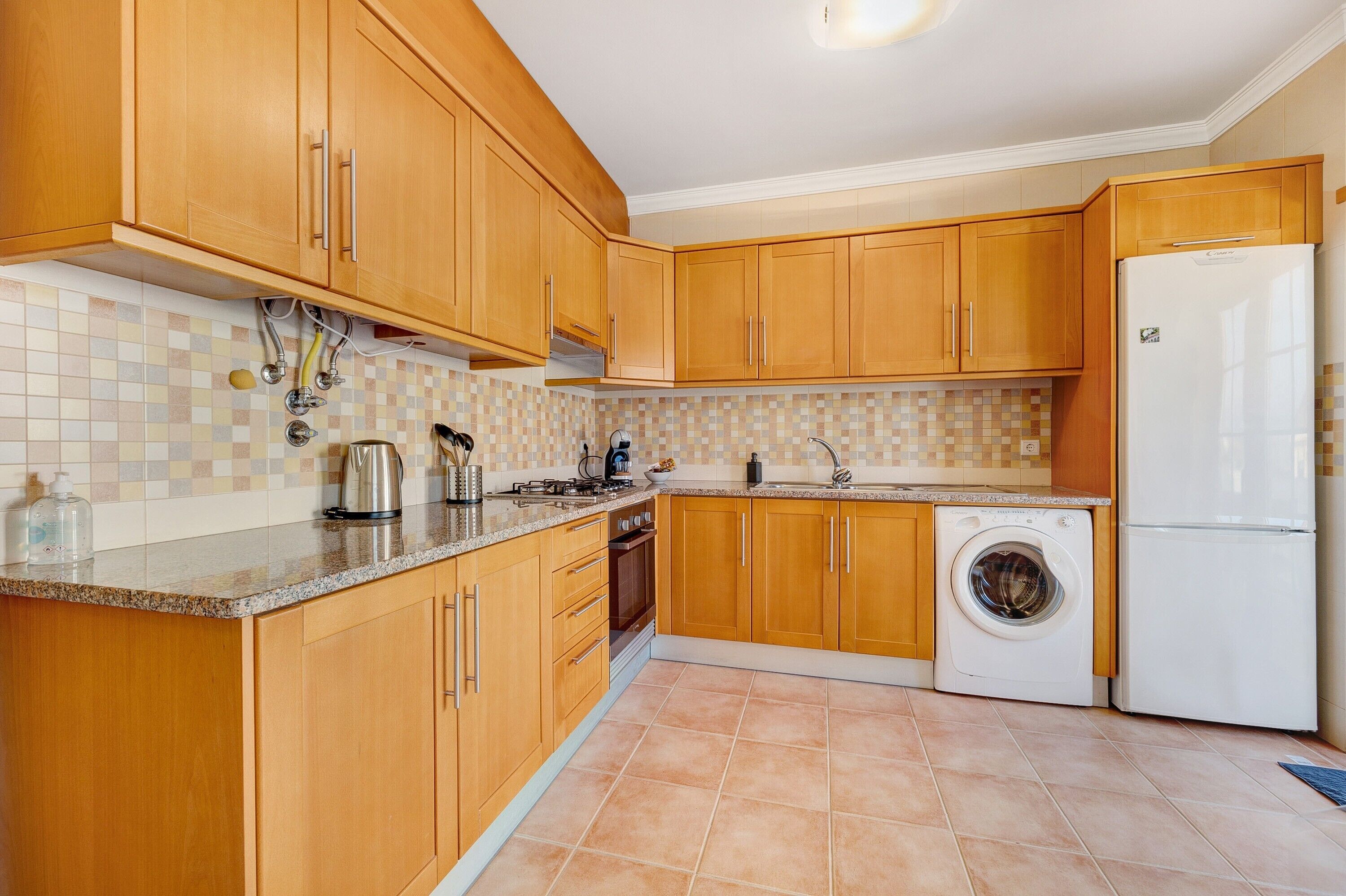 A kitchen with wooden cabinets, a washing machine, a refrigerator, and a tiled backsplash.