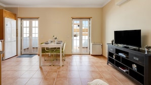 A kitchen with a refrigerator, a dining table with chairs, a TV on a stand, and a sliding glass door leading to a balcony. - Holiday Apartment "Tourismer Centro" in City Center with Shared Terrace & Wi-Fi (Lagos)