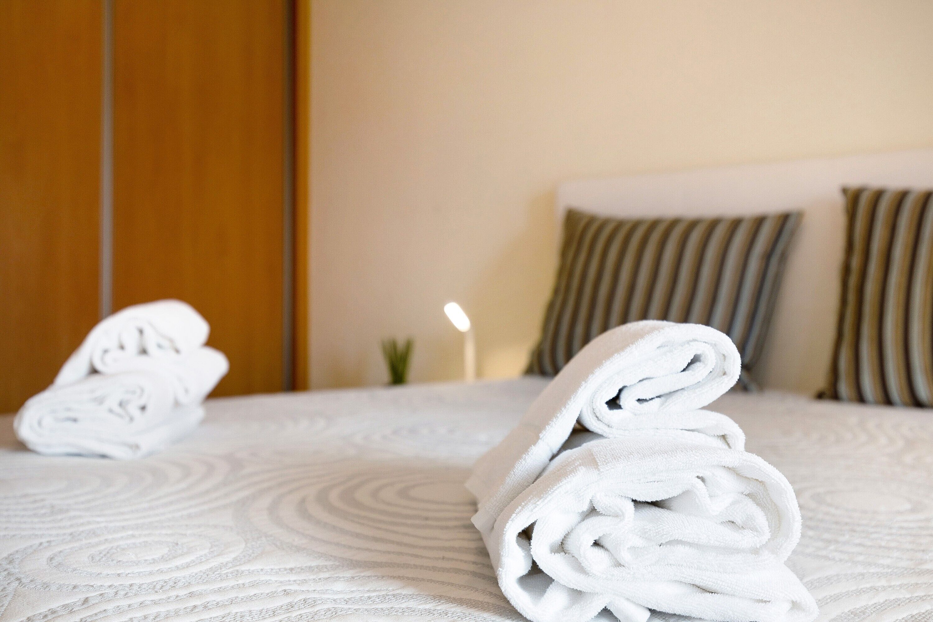 A neatly made bed with rolled white towels, a wooden wardrobe, and striped pillows.