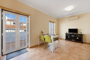 A room with a dining table, chairs, a TV, and a sliding door leading to an outdoor area.