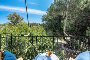Un balcón con una mesa, un frutero y vistas a árboles y colinas.