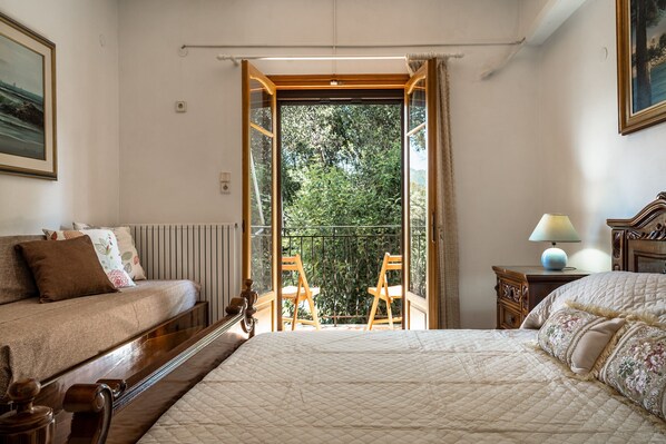 Un dormitorio con una cama grande, una cama más pequeña, un balcón con sillas y vistas a la vegetación.