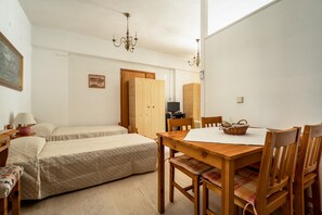 A room with two beds, a wooden dining table, chairs, a television, and a painting on the wall.