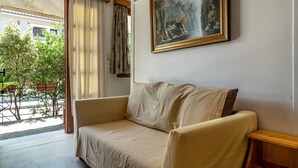 Een kamer met een beige bank, een schilderij aan de muur en uitzicht op groen.