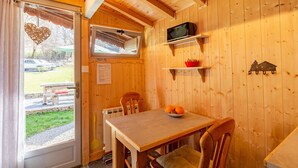 A wooden interior with a dining table, chairs, a television, and a window with a view of the outside. - Chalet "Sauvage" with Mountain Views, Private Terrace and Wi-Fi. (FAVERGES-SEYTHENEX)