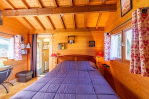 Ein Schlafzimmer einer Holzhütte mit Bett, Schreibtisch und Fenster mit Vorhängen.