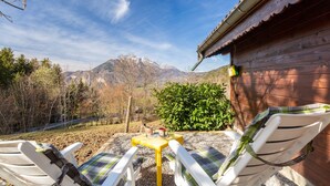 A patio with two white chairs, a small yellow table, and a view of mountains. - Chalet "Sauvage" with Mountain Views, Private Terrace and Wi-Fi. (FAVERGES-SEYTHENEX)