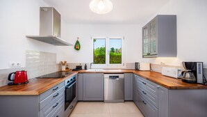 Una cucina moderna con mobili grigi, un piano di lavoro in legno, una lavastoviglie in acciaio inossidabile e un bollitore rosso.