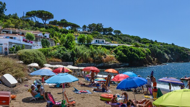 A beach with umbrellas, people relaxing, and buildings in the background.