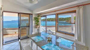 A room with a glass door leading to a balcony with a view of the sea and hills.