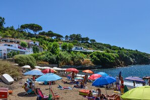 A beach with umbrellas, people relaxing, and buildings in the background.