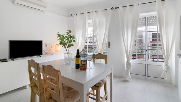 Un coin repas avec une table blanche, des chaises, un téléviseur, une bouteille et une plante.