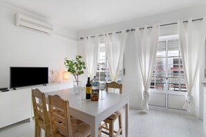 A dining area with a white table, chairs, a television, a bottle, and a plant.