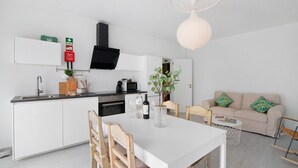 Une cuisine moderne avec des armoires blanches, une hotte noire et un coin repas comprenant une table blanche et des chaises en bois.