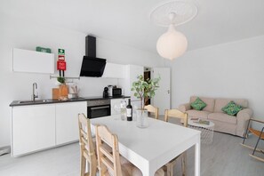 Eine moderne Küche mit weißen Schränken, einer schwarzen Dunstabzugshaube und einem Essbereich mit einem weißen Tisch und Holzstühlen.