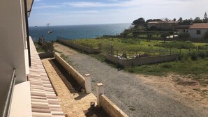 A view from a balcony overlooking a paved pathway leading to a grassy area with a fence, a building, and the sea in the background. - Holiday Apartment "Capo Rizzuto 3" with Sea View, Private Terrace & Wi-Fi (isola di capo rizzuto)