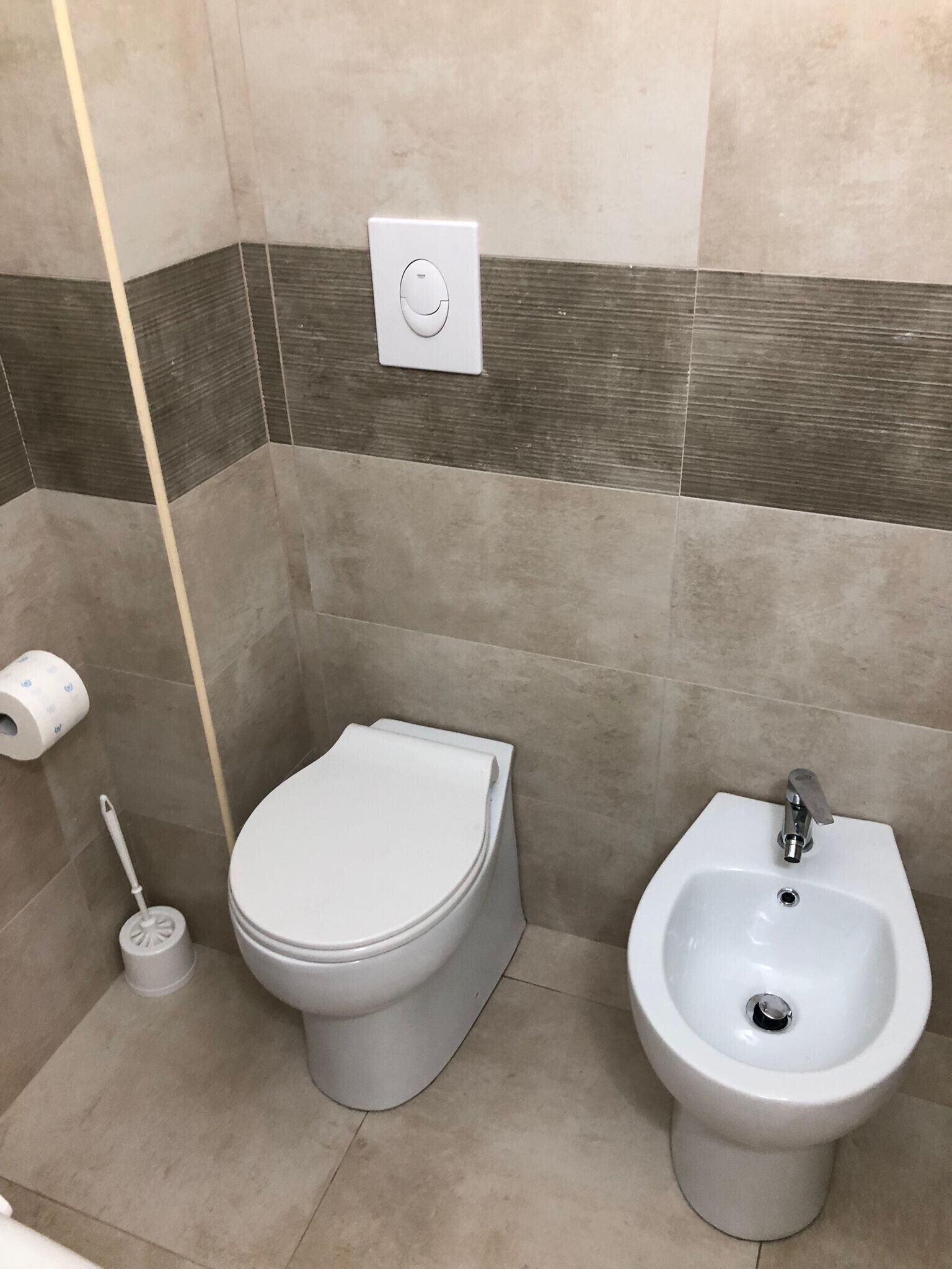 Ein Badezimmer mit Toilette, Bidet und Toilettenpapierhalter.