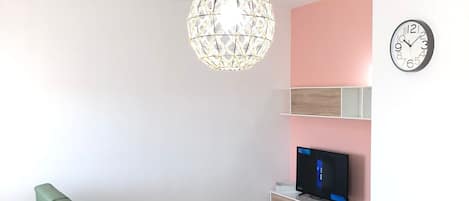 A modern living room with a green sofa, a white dining table, and a hanging spherical light fixture.