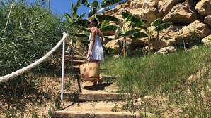 Una persona camina por un sendero de tierra con escalones, rodeada de vegetación y rocas.