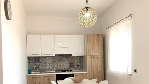 Una cocina moderna con armarios blancos, un salpicadero de azulejos y un comedor con mesa y sillas blancas.