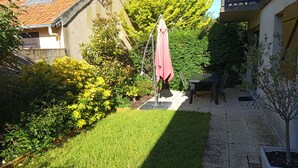 Une cour avec une pelouse, une table entourée de chaises, un parasol rose et une plante en pot.