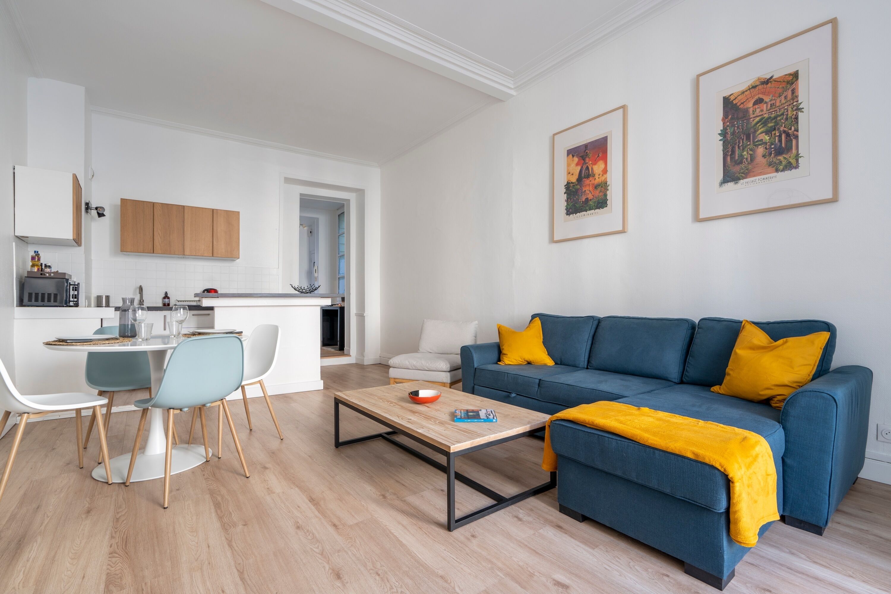 Un salon moderne avec un canapé bleu, une table basse en bois et un coin repas comprenant une table blanche et des chaises bleues.