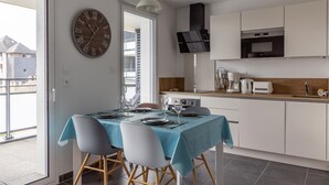 A modern kitchen with white cabinets, a built-in oven, and a microwave. There is a dining table with chairs and a clock on the wall.
