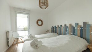 A hotel room with two beds, a white chair, a radiator, and a decorative wall with vertical panels.