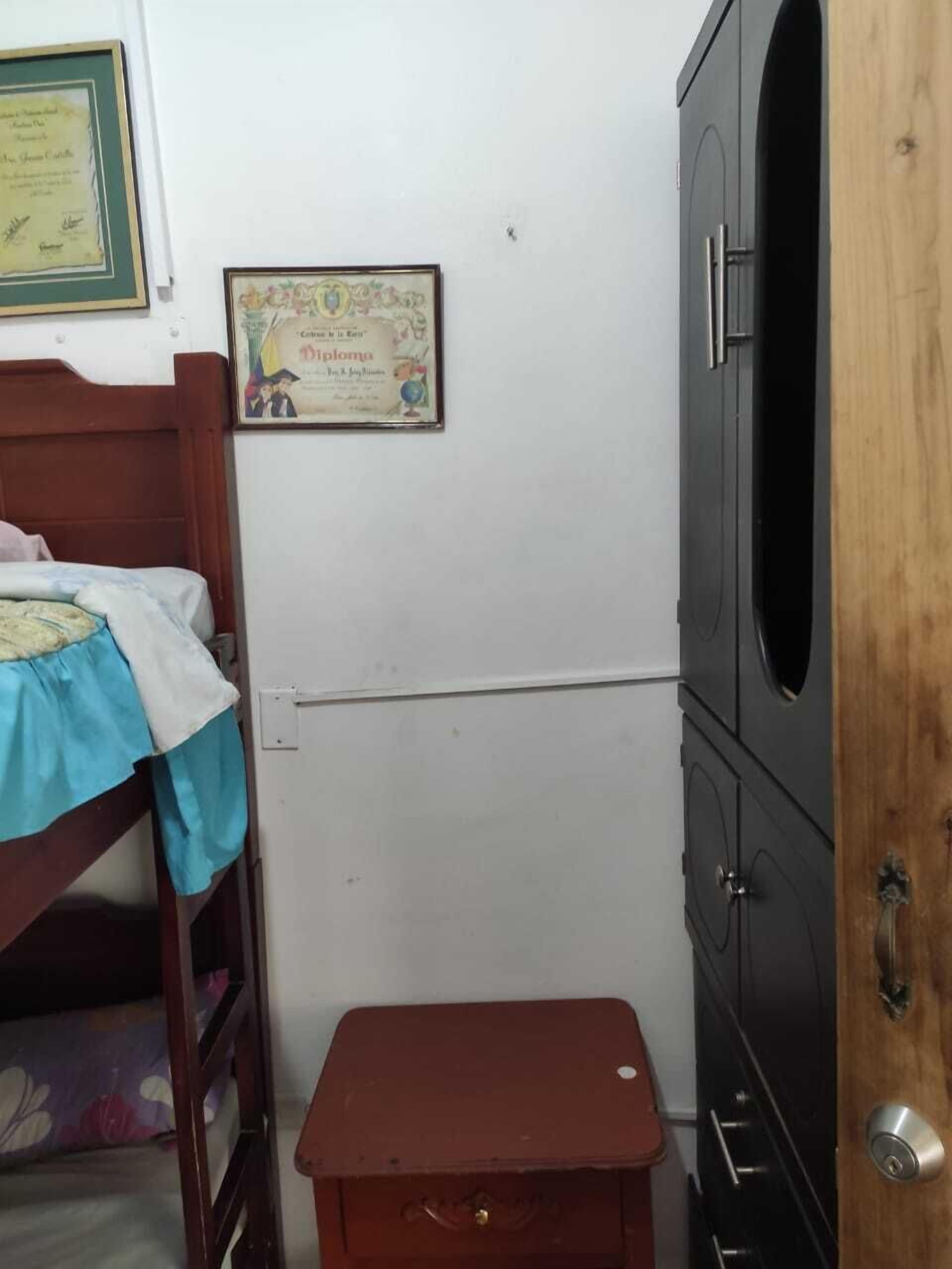 A bedroom with a bunk bed, a small wooden table, a wardrobe, and a certificate on the wall.