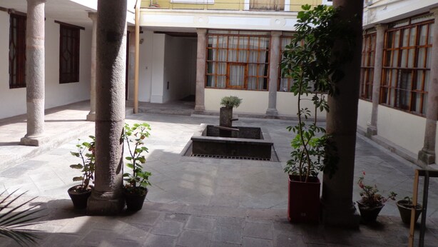 Un patio con columnas, plantas en macetas y una pequeña fuente.