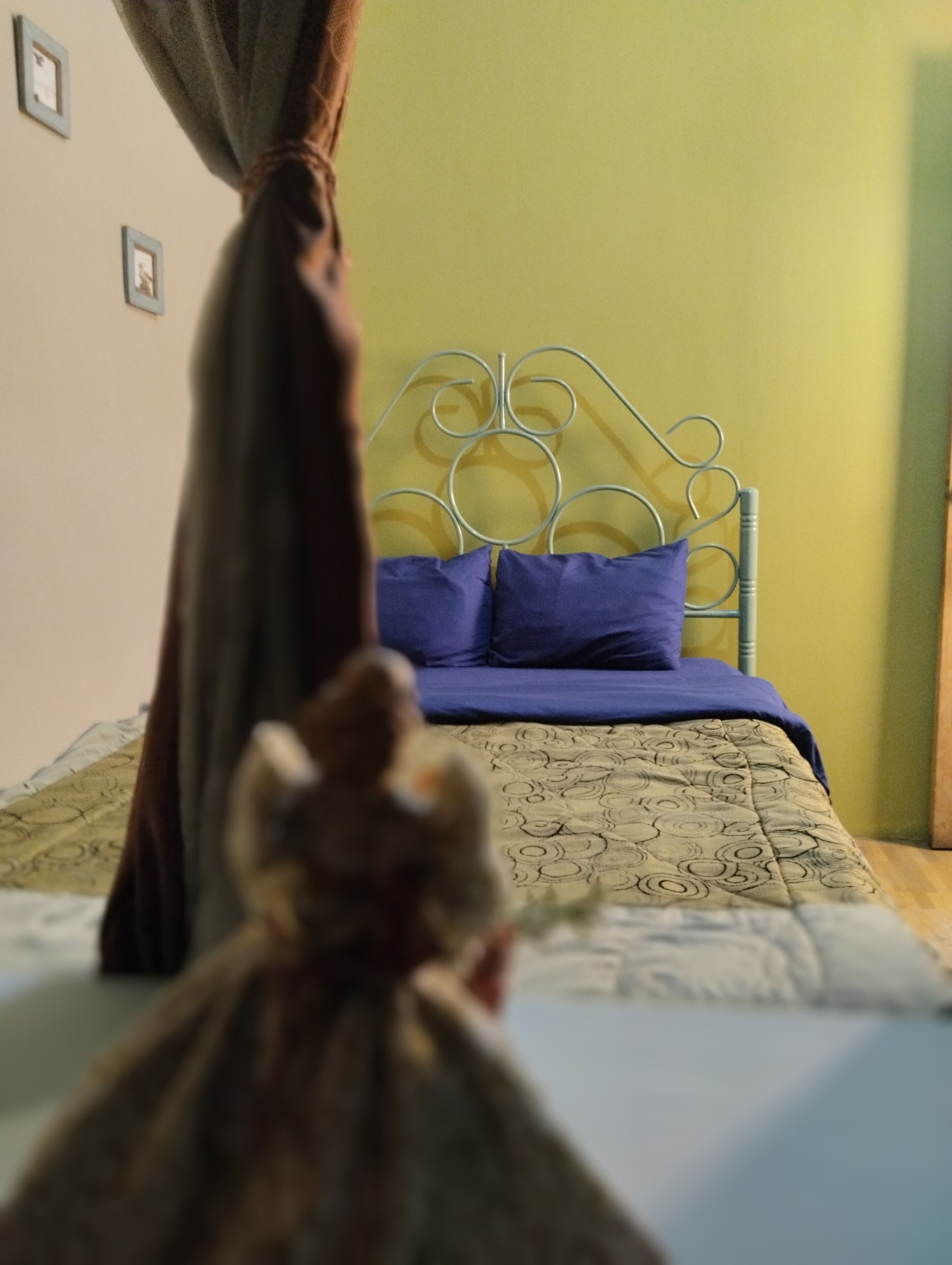 A bed with a metal headboard, a patterned bedspread, and a blue pillow.