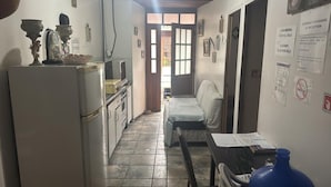 Cocina compacta con refrigerador, estufa y pileta. Un comedor con sillas se observa al frente. Una botella de agua azul está sobre la mesa.