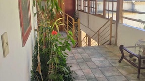 Un suelo de baldosas, una escalera, una barandilla de madera y una planta con flores rojas.