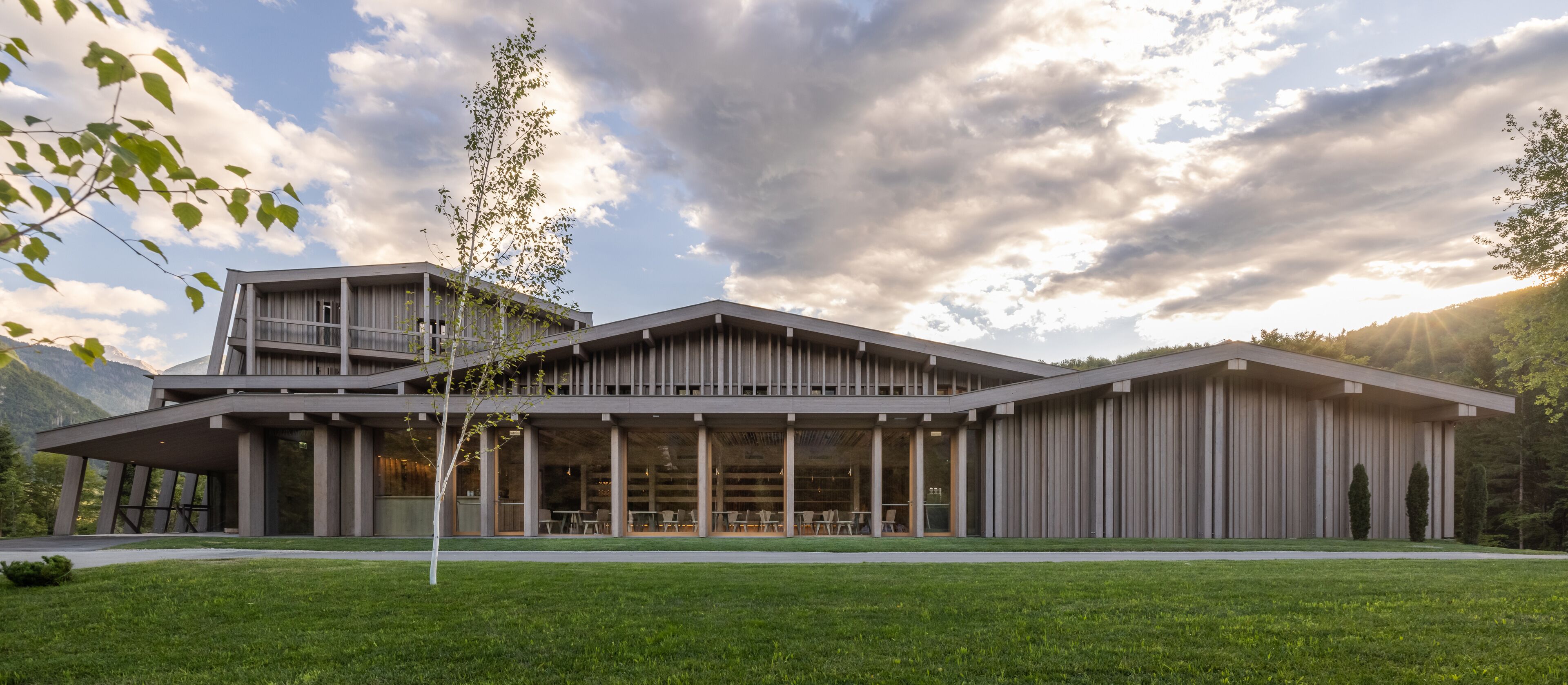 Un bâtiment moderne doté d’un toit plat, de grandes fenêtres et d’un espace extérieur couvert aménagé avec des sièges.
