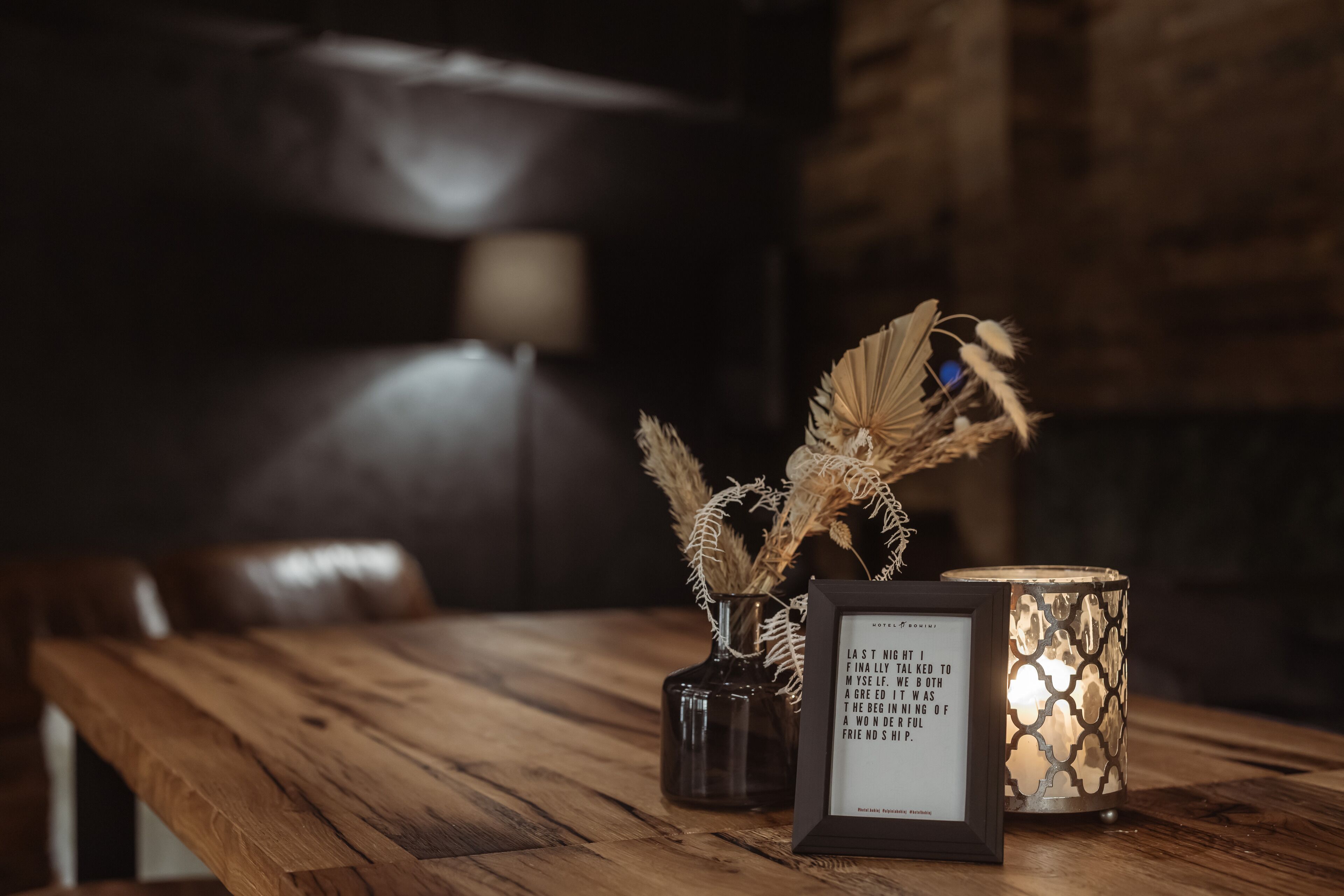 A wooden table with a framed quote, a vase with dried plants, and a patterned candle holder.