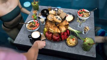 A breakfast buffet with various pastries, fruits, and beverages on a table by a pool.