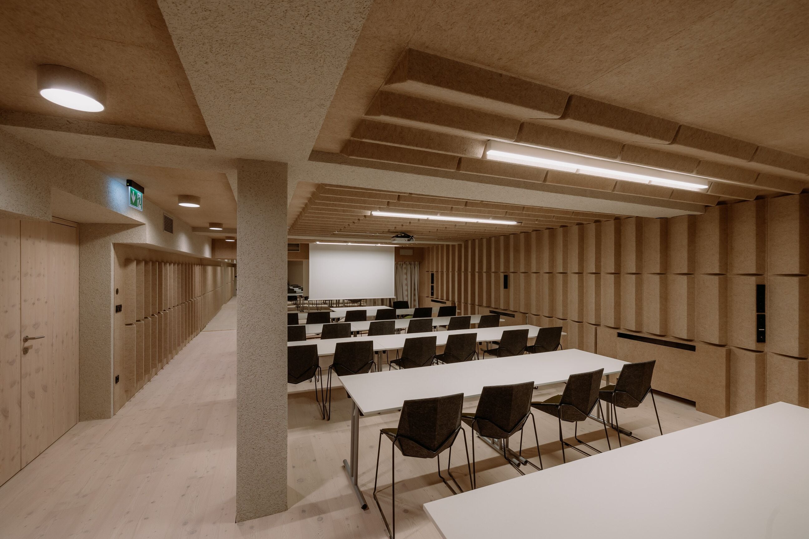 Ett konferensrum med vita bord och stolar, en projektorduk och en väggpanel av trä.