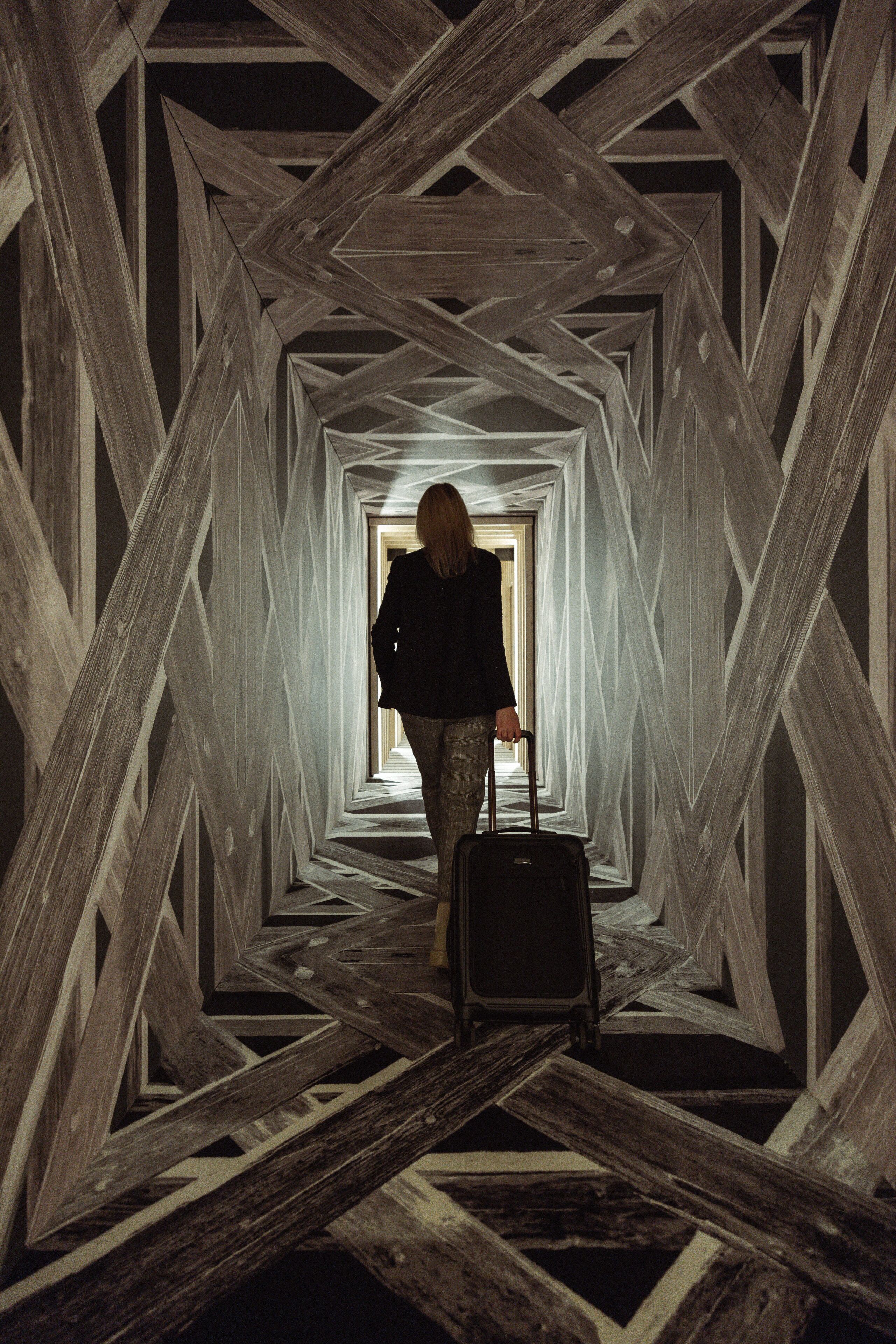 Une personne marchant dans un couloir, une valise à la main, entourée de structures géométriques en bois.