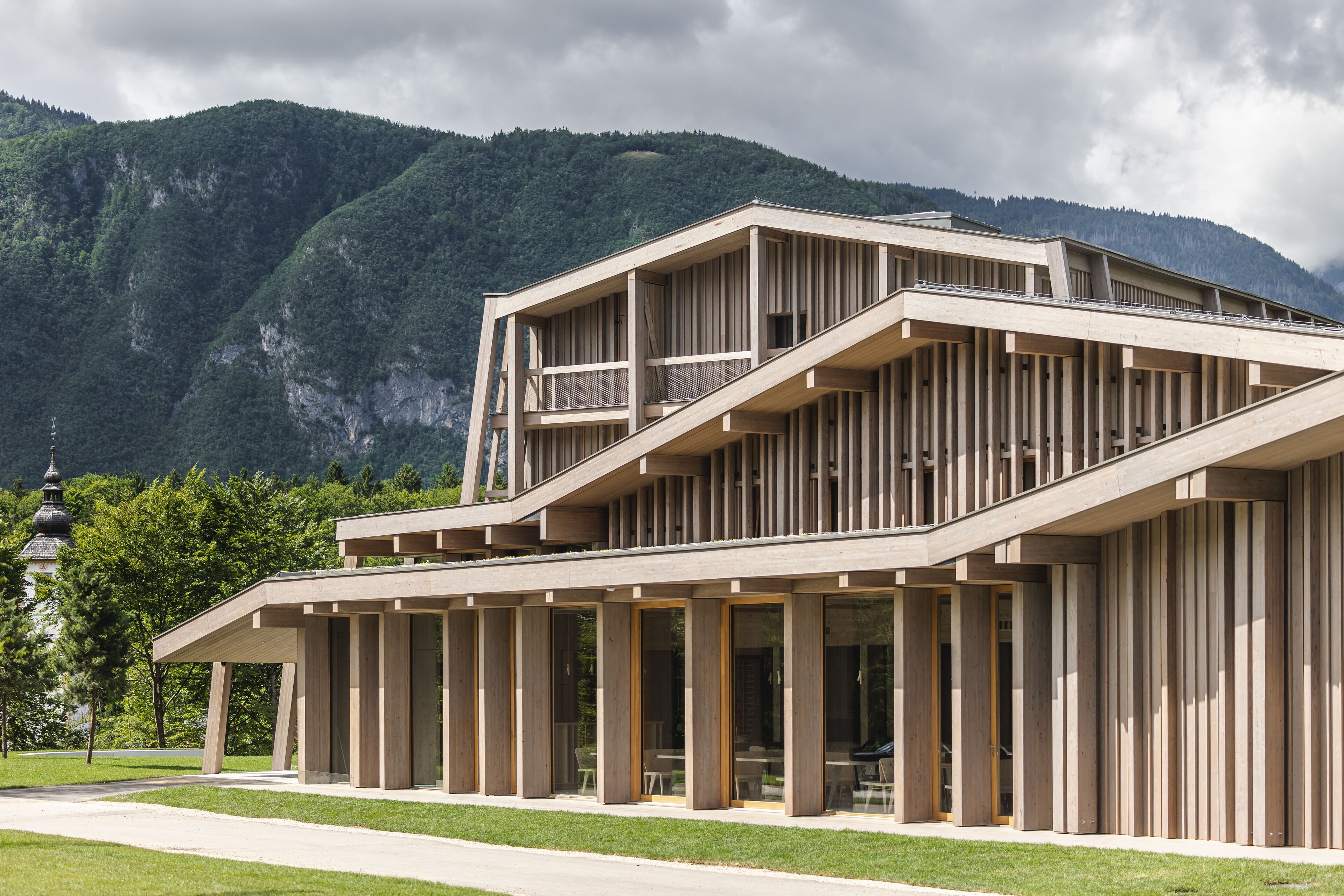 A modern building with a flat roof and large windows, set against a mountainous backdrop.