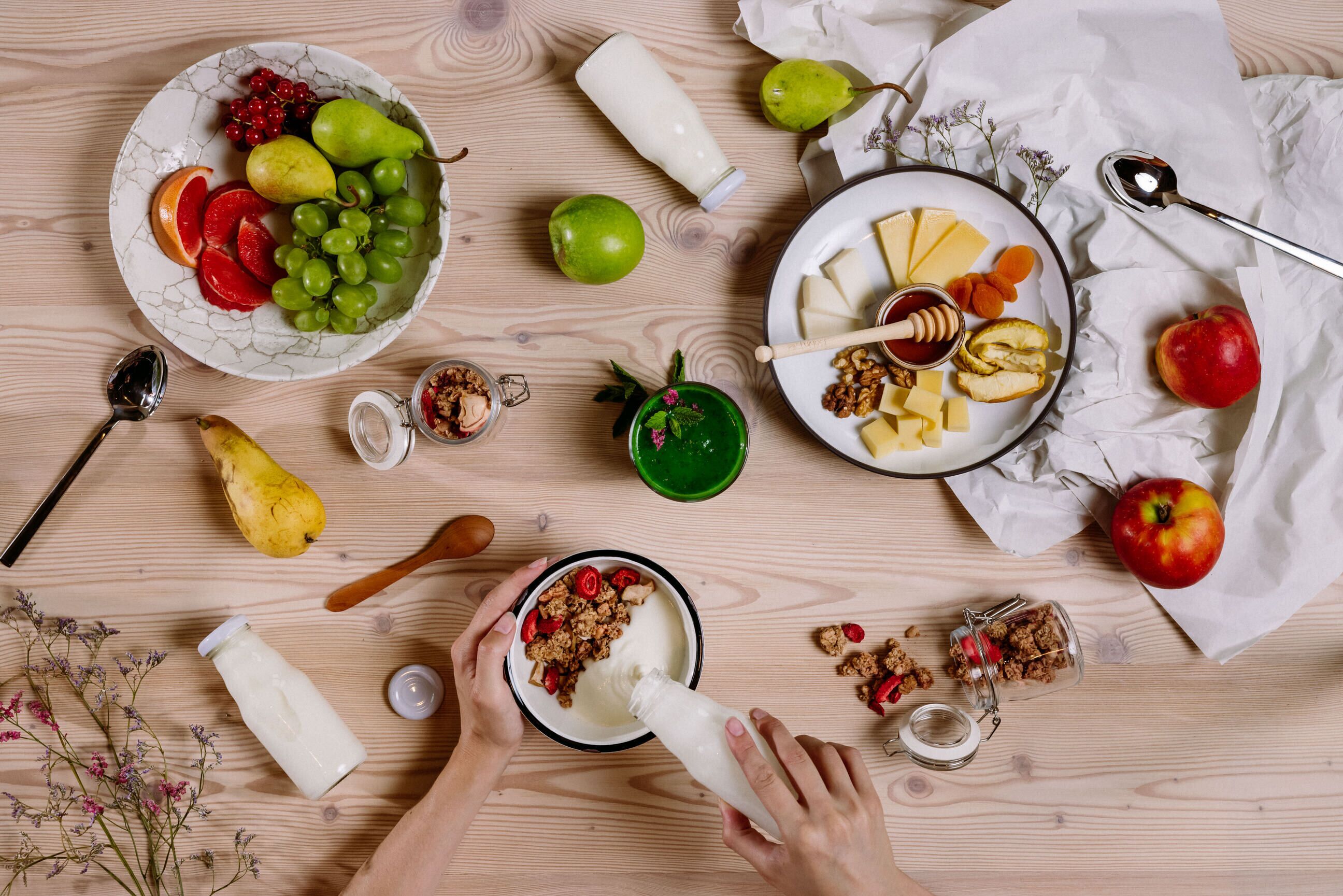 Uma mesa de madeira com diversos alimentos e uma pessoa servindo bebida em uma tigela.