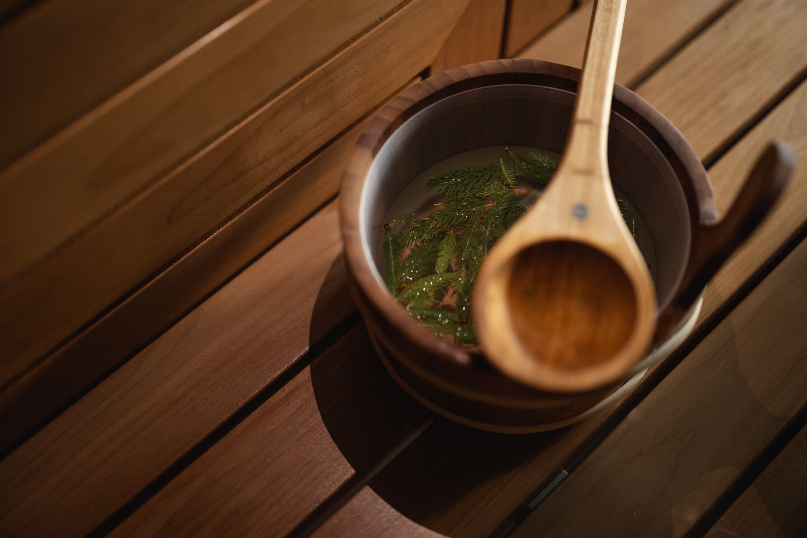 A wooden table with a bowl containing a liquid and a wooden spoon.