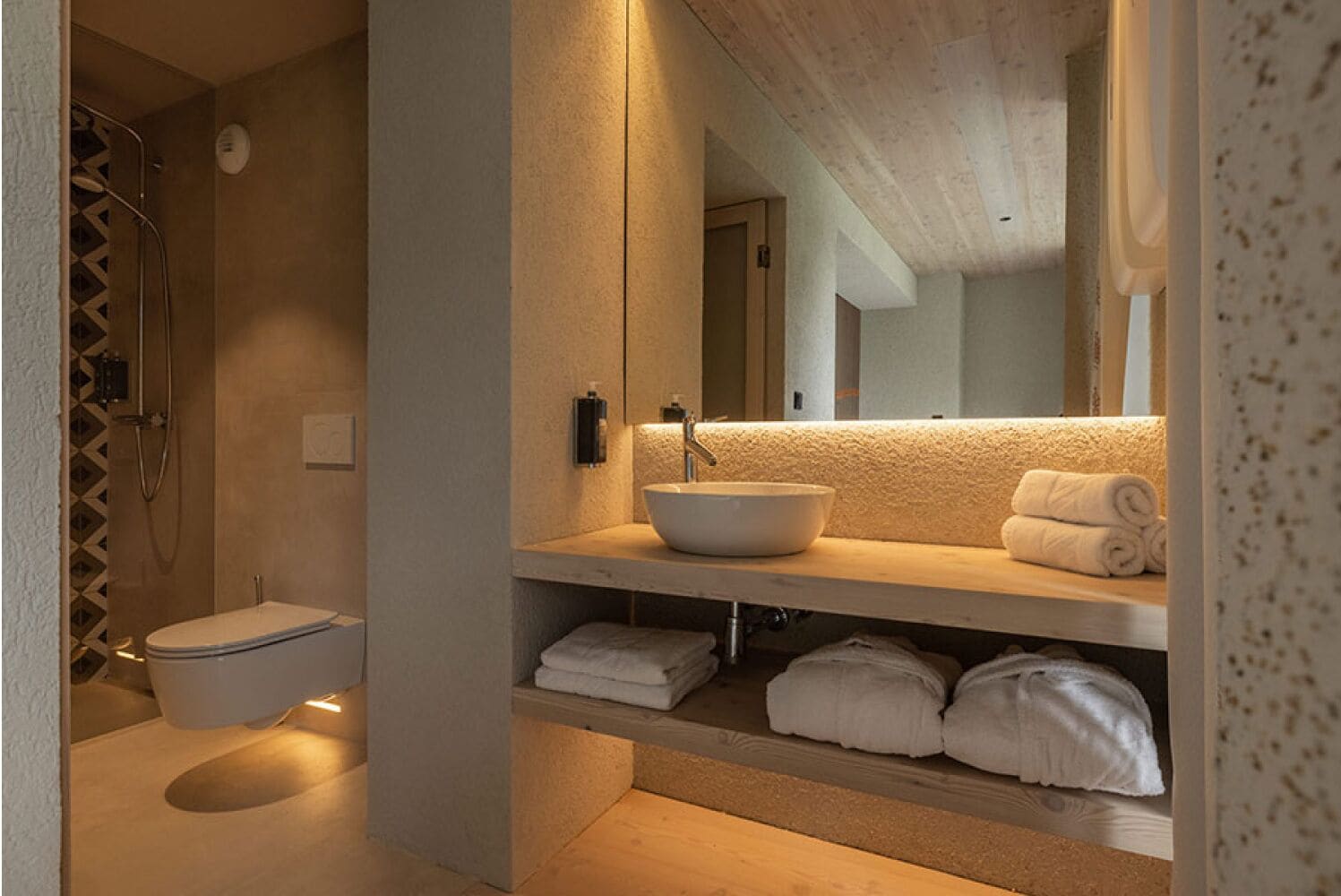 A modern bathroom with a walk-in shower, a toilet, a sink with a large mirror, and neatly folded towels on the counter.