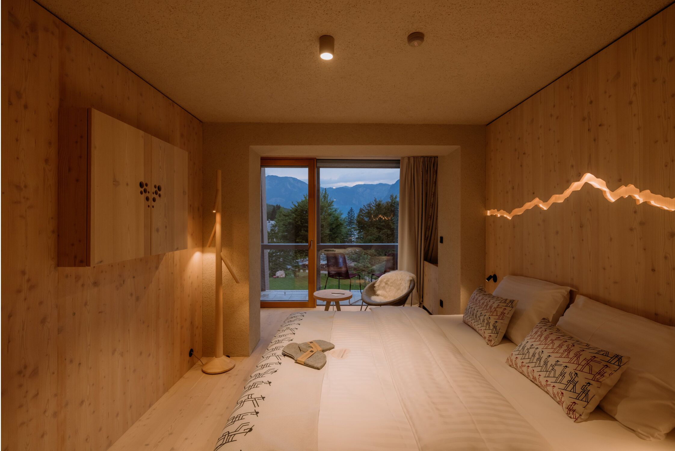 Una camera da letto con un letto grande, pareti in legno, vista sulle montagne e un tavolino con una sedia.