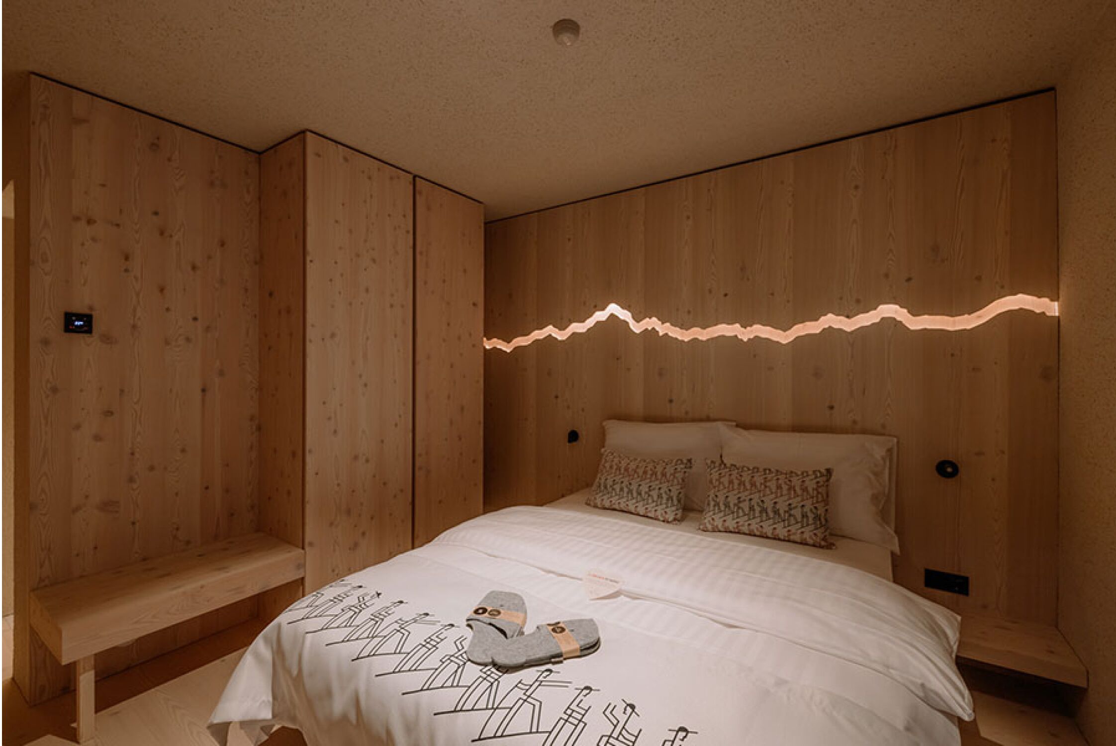 A wooden-paneled room with a bed, a bench, and a wall-mounted light.