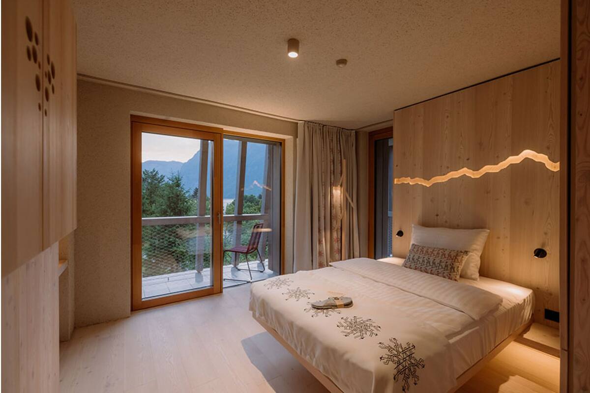A bedroom with a large bed, a sliding glass door leading to a balcony, and wooden paneling on the walls.