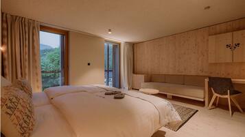 A modern bedroom with a large bed, a sofa, and a chair. There is a window with curtains, a wooden wall, and a ceiling light.