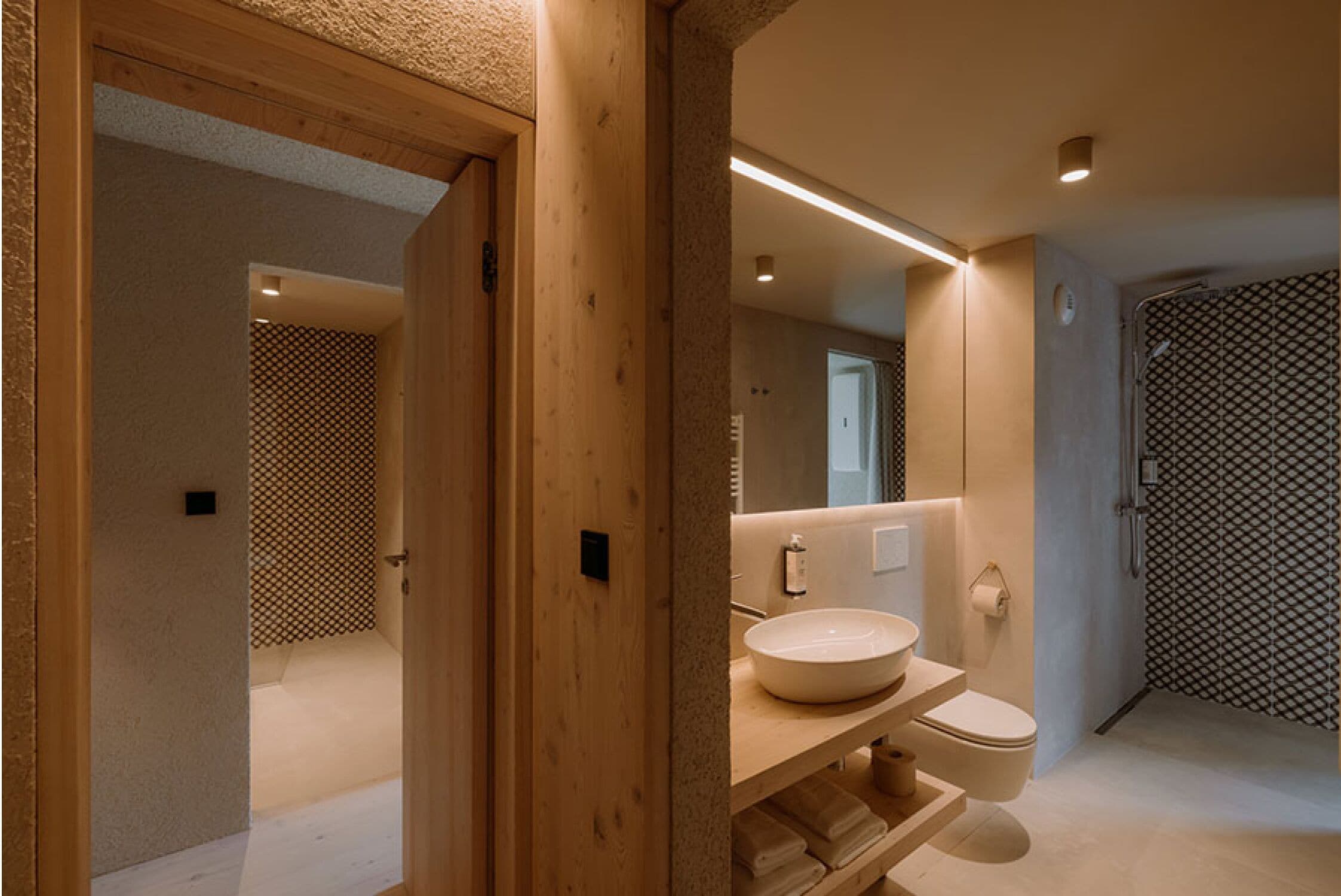 Un baño moderno con tocador de madera, un espejo grande y una ducha a ras de suelo con un revestimiento de pared estampado.