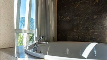 A modern bathroom with a freestanding bathtub, a window with curtains, and a dark marble wall.